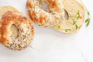 Close top down view on halved poppy seed bagles with green pea sprouts on white marble tabletop with copy space