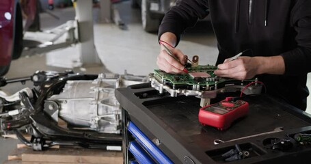 Mechanic working on disassembled electric car engine using a voltmeter. Concept of EV maintenance and repair in an auto service workshop. EV repair concept. Auto Service, Electric vehicle engine