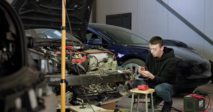Mechanic working on car engine repair at an auto service center. Focus on electrical system and precision tools in a garage setting. Mechanic works with car electrics - electrical wiring, voltmeter