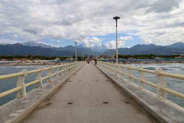 The famous pier in Forte dei Marmi, Italy which reaches out to the Ligurian sea. Located on the coast of the Tuscan region in Italy.  Few unrecognisable people in the far background.