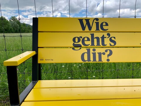 Schild - Beschriftung auf Sitzbank gelb" Wie geht es Dir? " Frage in englisch