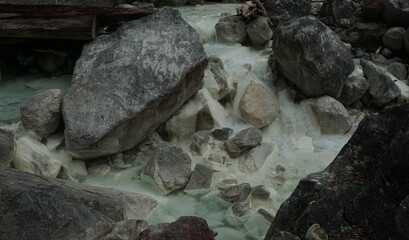 A clear river with hot sulfur water flows through the rugged landscape of the Sorikmarapi volcano area, North Sumatra, Indonesia.