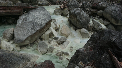 A clear river with hot sulfur water flows through the rugged landscape of the Sorikmarapi volcano area, North Sumatra, Indonesia.