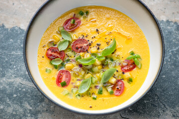 Bowl with chilled gazpacho made of sweet corn, yellow tomatoes and bell peppers, horizontal shot on a grey granite background, middle closeup