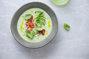 Bowl of chilled cucumber and green basil soup, top view on a grey granite background, horizontal shot