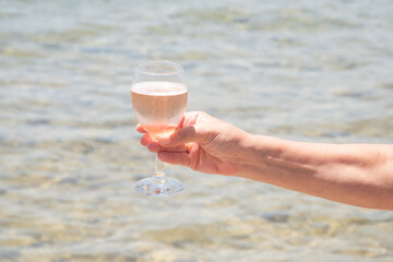 Woman hand holding a glass of champagne on the beach closeup