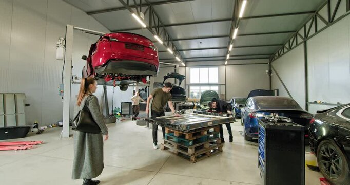 Technicians working on electric vehicles in a well-equipped auto repair shop. The image highlights battery modules and various cars being serviced. Electric car. Pack of battery cells module