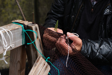 Hands of an old sailor sewing a fishing net. Horizontal photo.