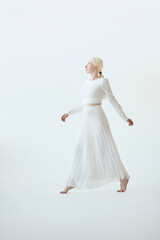 Pretty albino teen girl, beautiful barefoot unique model in white walking on tip toes in white studio background. Inclusive unusual natural beauty, inclusion, albinism, vertical full body photo.