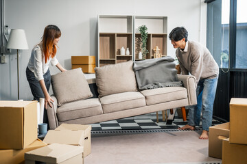  A young couple happily moves furniture together in their new home. They work as a team, lifting...