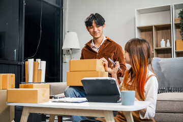 A young couple works from home, packing orders and managing their online store. They use technology and teamwork to run their business, smiling while fulfilling customer orders.