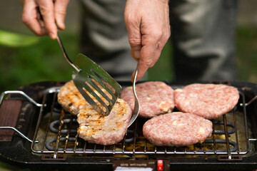 Man grilling burger meat on barbecue grill close up, smoke coming out of the grill, male person flipping burgers on a grill