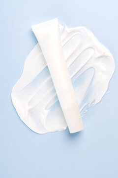 White squize tube of face or hand cream and sample texture in on blue background. Cosmetic laboratory research.