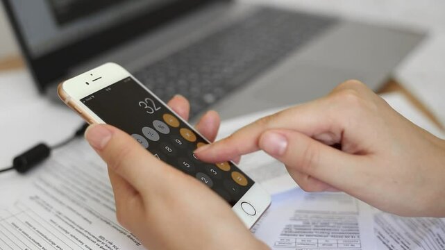 woman calculates utility bills using a calculator on her phone. close up