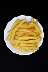 French fries in a white plate on a black background. Delicious fried potatoes.