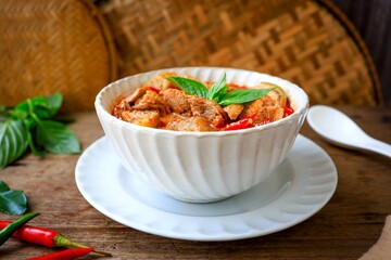 Thai spicy red curry add spicy red curry paste and  coconut milk in white bowl on thai style bamboo basket and wooden background, thai food, thai cuisine