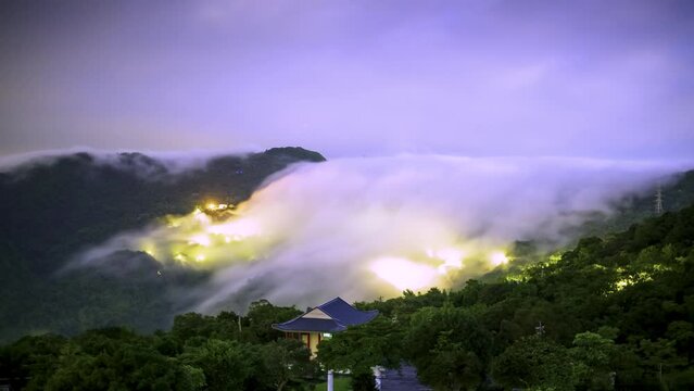 Clouds in the midnight sky. Cloud waterfall on the top of the mountain. View of the mountains surrounding Emerald Reservoir. Xindian District, Taiwan.