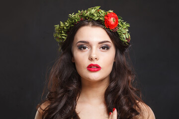 Naklejka premium Glorious young woman with floral head wreath looking at camera while standing against black background