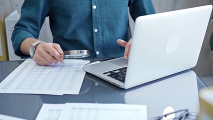 Fototapeta premium Businessman or professional auditor is analyzing data sheets. Auditing financial documents with magnifying glass and laptop. Finance audit and business