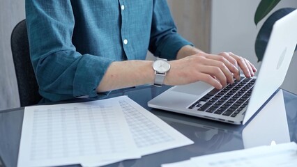 Professional casual dressed businessman is working on laptop at office grey and glass desk. Close-up of an adult's hands typing on a keyboard. Business people