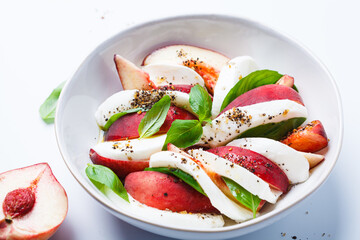 Caprese salad with peach, basil and mozzarella, white background.