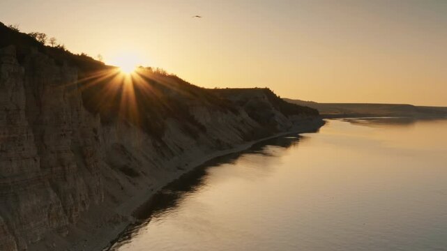 The sun's rays break through on the horizon. Rocky steep banks of Cretaceous and Paleogene deposits. Beautiful aerial drone shot of a flying bird