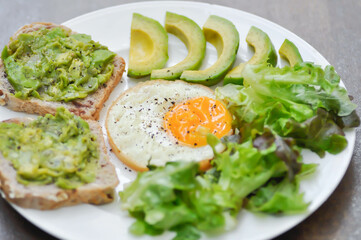 bread with mashed avocado topping ,sunny side up egg with lettuce and avocado