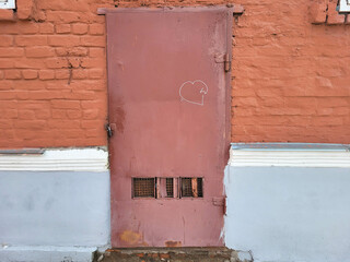 On the red brick facade there is an iron red door with a painted white heart