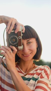 vertical shot. the girl presses the button. a young girl with a camera takes a picture. Fashionable and attractive beautiful woman with an analog film camera in her hands.  travel and vacation.

