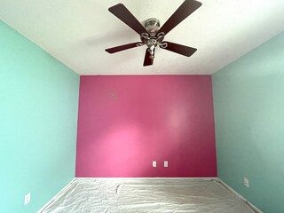 A brightly painted bedroom with pink and teal colored walls. The floor is covered with drop cloths...