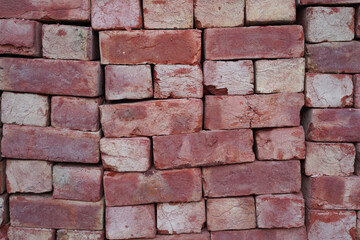 Red bricks wall backdrop. Hand-formed red bricks stacked in a stack. Close-up, rough texture, background.
