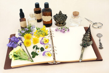 Spring flowers, herbs and wildflowers used in natural herbal medicine remedies with notebook and essential oil bottles for naturopathic essences on hemp paper background.