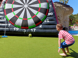 a blond boy, on summer vacation, plays hitting a huge inflatable target with a ball