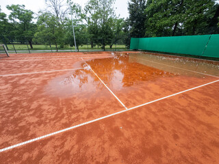 Fototapeta premium Wet clay tennis court with puddles during the rain. Outdoor tennis season. Spring rain on courts. All practices and match are cancelled