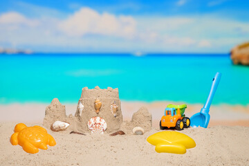 Sand castle and child toys on sand beach at tropical resort. Family vacation. Relax on the beautiful sea coast beach. Azure water on the ocean, sea coast resort. Summer holidays. Blue sky. Copy space.
