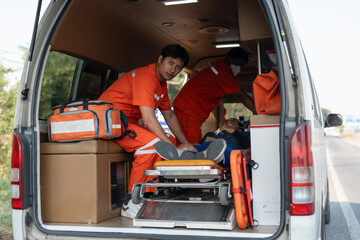 Team of Asian male EMS paramedics or emergency medical technicians in orange uniforms helping patient to ambulance from road accident.