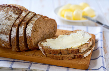 slice home baked rye sourdough bread with butter on a wooden table.