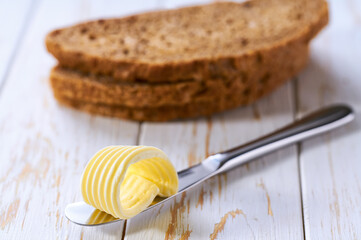 Close up butter on a knife with sliced rye bread, on a kitchen table.