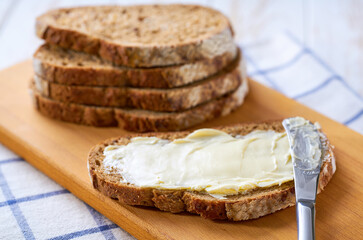 Tasty cut multigrain sourdough bread with fresh butter on a white wooden table.