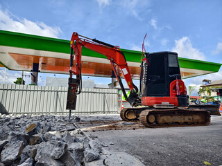 Excavator using hydraulic hammer for breaking concrete at a construction site