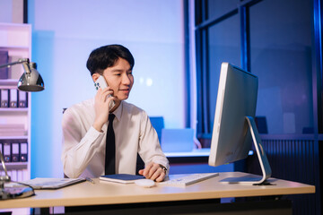 Overtime work concept, Handsome asian business man working overtime sitting at desk using computer and doing overtime project