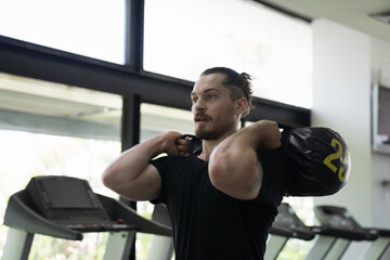 Man doing workout exercise with heavy  weight sand bag in gym. Man training hard in sport gym. Man exercising holding sand bag in fitness gym. Sport fitness concept