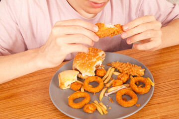 Caucasian man eating fried chicken wings, potato chips, onion rings and chicken wings by hand from a gray plate on a wooden table