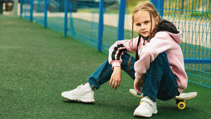 Fototapeta premium child skater, kid girl sitting relax at skatepark with skateboard. extreme sports in skate park