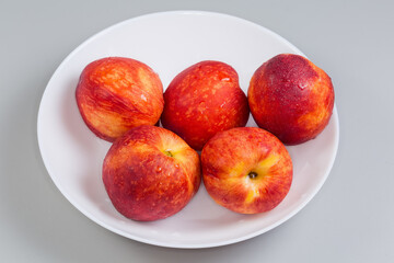 Ripe nectarines on white dish on a gray background