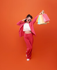 Happy pretty shopaholic woman carrying colorful shopping bags isolated on orange studio background..