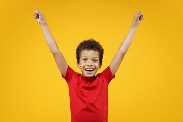 Studio shot ot cute little champion, happy excited African American schoolboy rasing his hands up...