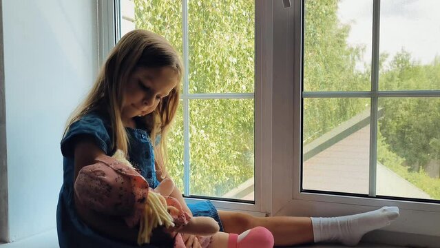 little girl hold doll and play mother daughter game, sit on the windowsill, role-playing