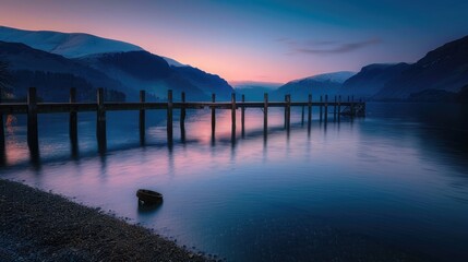 Obraz premium A tranquil lakeside scene at dusk, with a wooden pier extending over the water and mountains in the background.