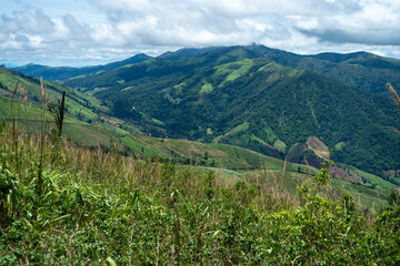 A scenic summer landscape unfolds beneath a vibrant blue sky, with lush green mountains and rolling hills in the distance